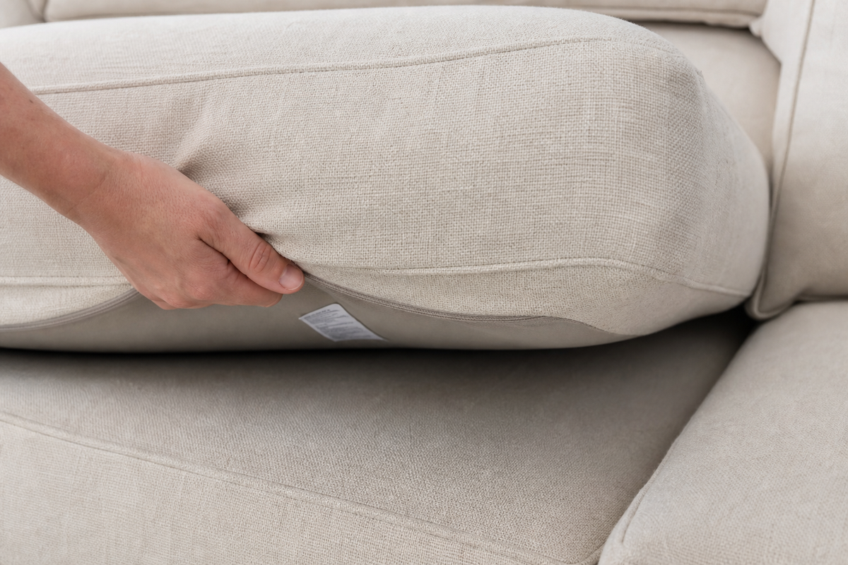 Checking the upholstery care label beneath a couch cushion before spot cleaning.